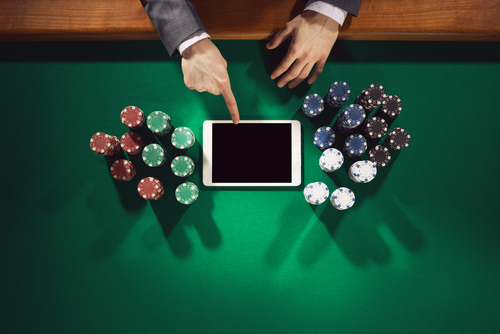 homme touchant une tablette informatique avec des jetons de casino tout autour